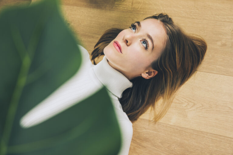 thoughtful-woman-lying-floor-near-plant