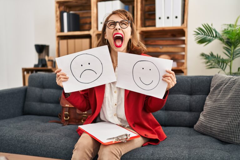 Young beautiful woman working on depression holding sad to happy emotion paper angry and mad screaming frustrated and furious, shouting with anger looking up
